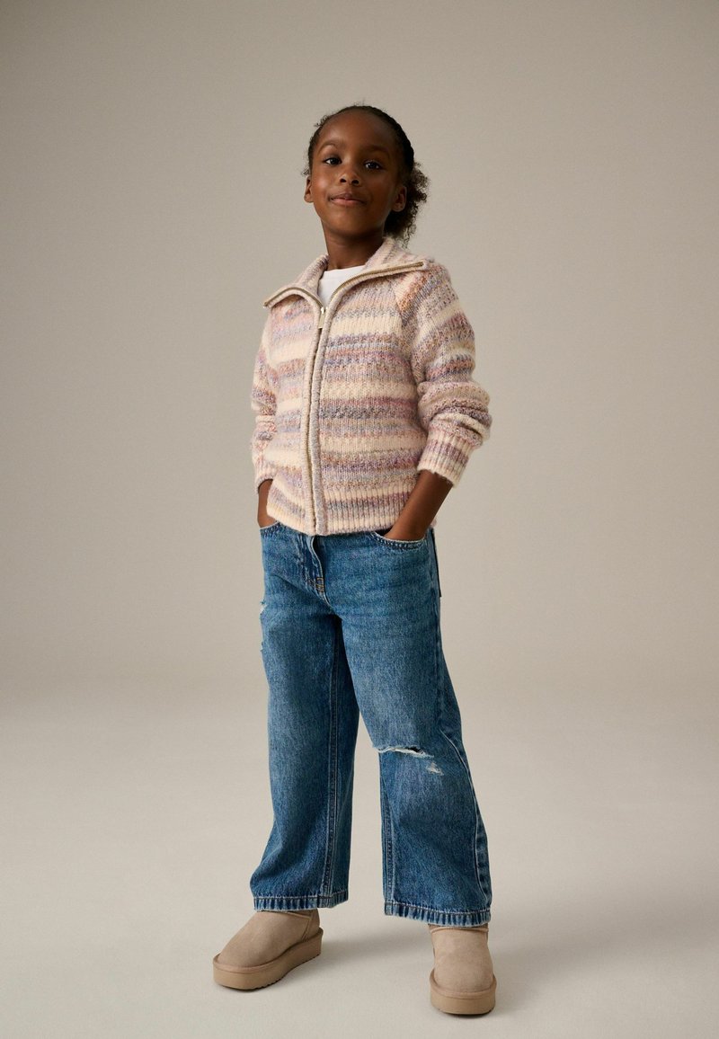 Mehrfarbiger gestreifter Strick-Zipfel-Pullover mit gerippten Kanten, kombiniert mit lockeren, ausgebleichten blauen Jeans und beigefarbenen Slippern.