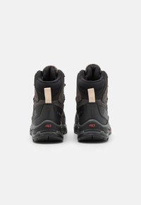 Svarta vandringsskor med en strukturerad överdel, utrustade med en vadderad krage, dragflik och röda detaljer på sulan. Robust design för utomhusbruk.