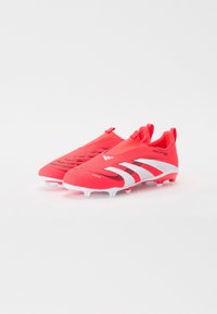 Bottes de football rouges au design élégant de type chaussette, avec des accents blancs, une tige texturée et une semelle à crampons pour une adhérence améliorée sur le terrain.