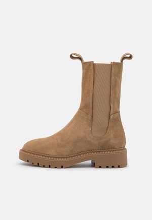 Botte en daim couleur cognac mi-mollet avec semelle épaisse, panneaux latéraux élastiques et languettes de tirage sur fond blanc.
