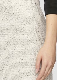 Texturiert, off-weißes Gewebe mit grauen Sprenkeln; körpernahe Form von der Taille bis zur Hüfte, mit einer Hand, die auf dem Material ruht.
