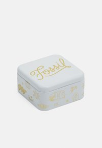 Quadratische Metalldose mit einem weißen Grund und goldenen Grafiken, einschließlich des "Fossil"-Logos, Blumen und dekorativen Mustern. Glatte Oberfläche.