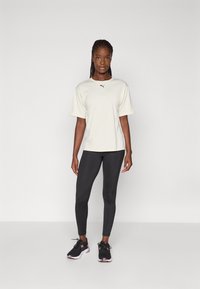 Lichtbeige T-shirt met korte mouwen en een zwart logo, gecombineerd met zwarte legging en zwarte sportschoenen met roze accenten. Eenvoudig ontwerp, slim fit.