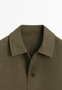 Olive green collared shirt with subtle checkered pattern and a single visible black button near the collar.