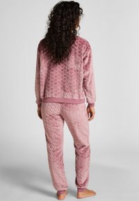 Różowy pluszowy dres z fakturowanym, falistym wzorem. Kurtka ma ribbowe wykończenie, a spodnie mają elastyczne mankiety.