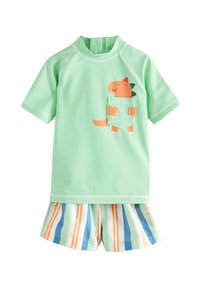 Lys grøn kortærmet rash guard med en tegneserie dinosaur lomme. Parret med stribede shorts i blå, orange, og grønne nuancer.