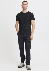 Svart bomull T-shirt tillsammans med svarta cargobrallor med sidofickor. Outfiten fulländas med silvriga sneakers.