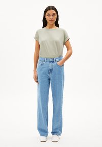 T-shirt verde chiaro a maniche corte abbinato a jeans a gamba larga blu chiaro a vita alta. Scarpe bianche completano l'outfit. Sfondo semplice.