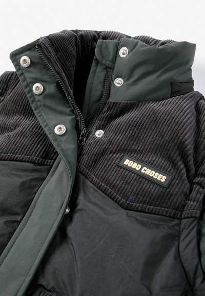 Veste matelassée noire avec partie supérieure en velours côtelé, boutons-pression argentés, fermeture éclair et une étiquette indiquant "BOBO CHOSES" sur la poitrine.