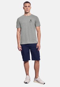 Šedé bavlněné tričko má krátké rukávy a na hrudi grafiku slunce a vln; je spárováno s námořnickými cargo šortkami s bočními kapsami.