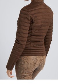 Brun vadderad jacka med en elegant design, försedd med horisontell quiltning och hög krage. Tyget verkar mjukt och slätt.