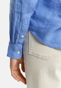 Lichtblauw linnen shirt met knoopmanchetten, gedragen over lichtbeige jeans met een achterzak. Geweven stof met een casual ontwerp.