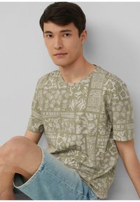 Olijfgroene T-shirt met korte mouwen en witte tropische patronen; ronde hals; gecombineerd met lichtblauwe denim shorts. Gladde textuur.