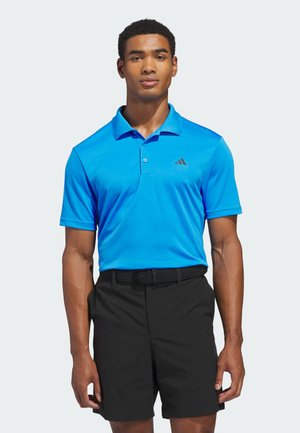 Blaues Polohemd mit Kragen und Dreiknopfleiste, mit kleinem schwarzem adidas-Logo; kombiniert mit schwarzen Shorts und einem schwarzen Gürtel.