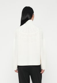 Sweater branco tricotado com colarinho alto, yoke com padrão texturizado e punhos e barra canelados. Ajuste descontraído, textura suave, design minimalista.