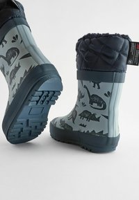 Wodoodporne gumowe kalosze w kolorze szarym z czarnymi wzorami dinozaurów, uzupełnione o pikowaną górę w kolorze granatowym i teksturowaną niebieską podeszwę.