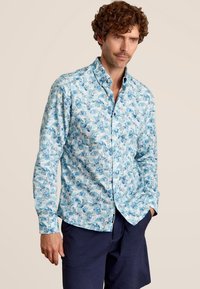 Lichtblauw overhemd met knoopsluiting, voorzien van een bladerenprint in donkerblauw, met lange mouwen en een kraag. Gemaakt in combinatie met marineblauwe shorts.