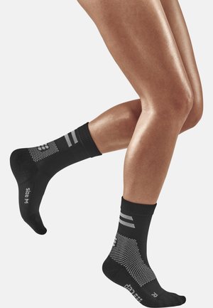Schwarze Sportsocken mit strukturiertem Design, die oben graue Streifen und einen gemusterten Abschnitt am Fuß aufweisen. Größe M an der Seite angegeben.