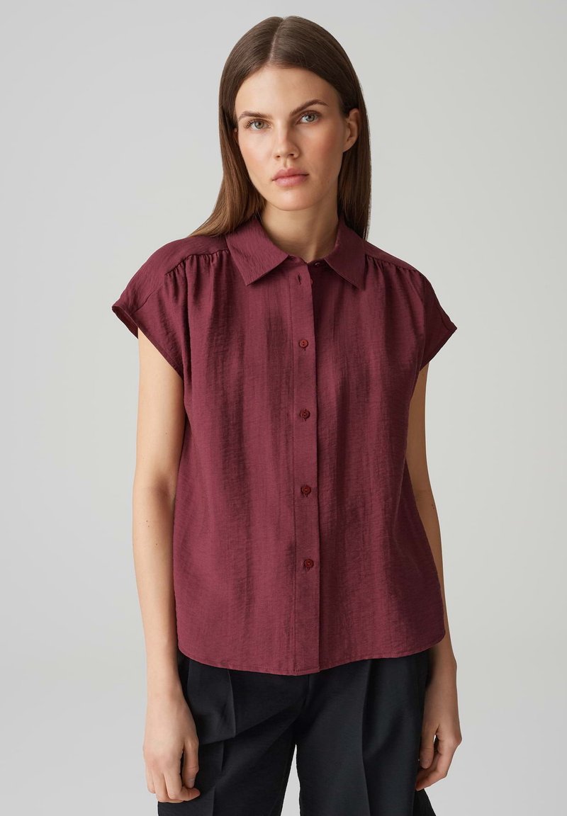 Bordeaux blouse met korte mouwen, knoopsluiting aan de voorkant, lichtgewicht textuurstof, geplooide schouders en een klassiek kraagontwerp.