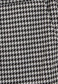 Črno-bela tkanina v vzorcu houndstooth, ki prikazuje ponavljajoči se geometrijski vzorec z ostrimi koti in teksturirano površino.