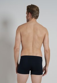 Boxer da uomo in cotone nero con cintura elastica, visti da dietro, indossati da una figura maschile con capelli corti e mossi.
