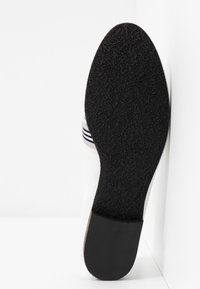 Semelle d'une chaussure en cuir noir avec une prise texturée et un talon contrastant, incliné en position verticale sur un fond blanc.