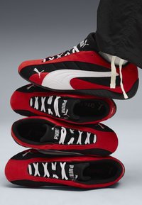Zapatillas rojas y negras apiladas, con un diseño de malla, detalles en blanco y cordones negros. Incluye el logo de Puma en los lados y en la lengua.