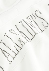 T-shirt bianco in tessuto con strass argento in rilievo disposti in un motivo, creando un elemento decorativo e testurizzato sul lato superiore.
