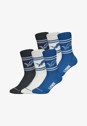 Vier paar sokken: zwart, wit en blauw met een geribbelde textuur. Elke sok heeft een blauw leeuwenlogo en contrasterende strepen nabij de bovenkant.