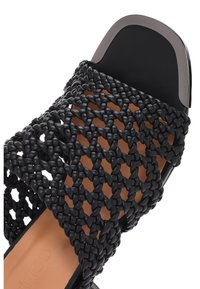 Sandalo nero open-toe con texture intrecciata, dettaglio metallico sul tallone e suola piatta con plantare liscio color tan.