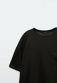T-shirt nero a maniche corte in tessuto leggero con scollatura rotonda e taschino sul petto, caratterizzato da una superficie testurizzata e una vestibilità rilassata.