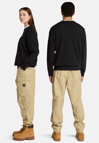 Felpa nera con maniche lunghe, abbinata a pantaloni cargo beige con tasche laterali. Entrambi sono indossati con stivali marroni stringati.