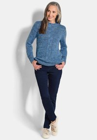 Maglione blu lavorato a maglia con motivi testurizzati, scollo rotondo e maniche lunghe, abbinato a pantaloni blu scuri e sneakers beige chiaro.