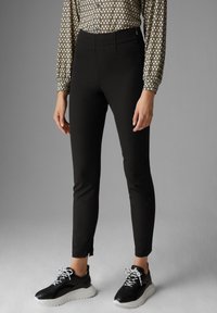 Zwarte op maat gemaakte broek met een slim fit, met een platte voorkant en subtiele zijslits aan de zoom. Gediend met zwart-witte sneakers.