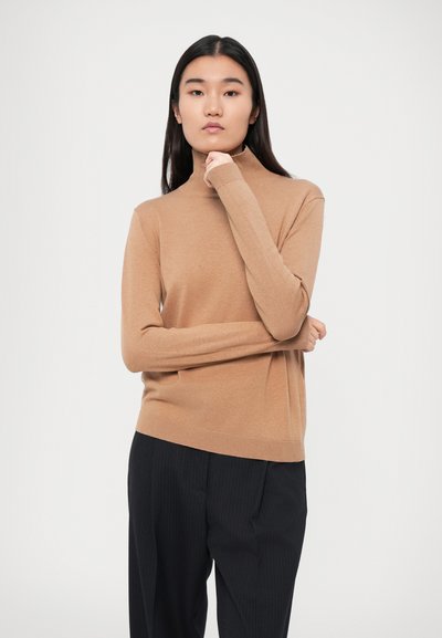 Hele pruuni, nõtkelt pehme kudumisega turtleneck-sviiter, pikki varrukatega, ribakujuline kaelus ja alläär, koos tumedate triibuliste pükstega.