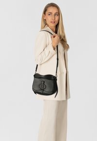 Schwarze Leder-Umhängetasche mit gewölbtem oberen Teil und dekorativem vorderem Verschluss. Verfügt über einen langen, verstellbaren Riemen und eine strukturierte Oberfläche.