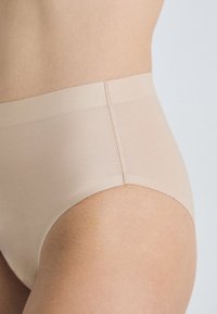 Beige hooggeremde onderbroek van zacht, gladde stof. Kenmerkt zich door een naadloze tailleband en een aansluitende vorm.