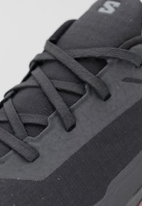 Gros plan de lacets de baskets noirs croisés sur un tissu et une matière supérieure synthétique texturée.
