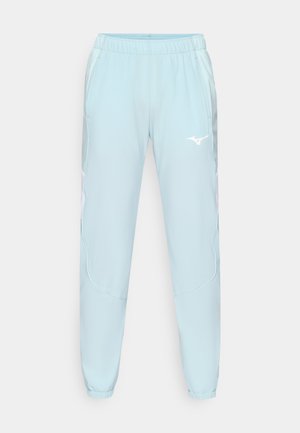 Lyseblå treningbukser laget av glatt stoff, med elastisk midje, tapered ben og en hvit logo på venstre lår.