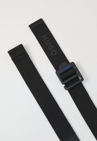 Cintura nera in nylon con fibbia in plastica, con il logo "HUGO" impresso sulla cintura. Texture liscia, lunghezza regolabile.
