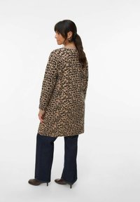 Cardigan long avec imprimé léopard en beige et noir, doté de manches longues et d'une coupe décontractée, associé à un jean flare foncé et des bottes à talons.