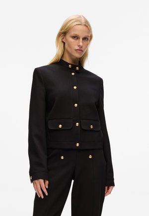 Black cropped jacket with gold-button accents, high collar, two front pockets, and smooth texture, paired with matching black pants.