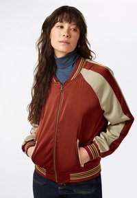 Red and beige bomber jacket with ribbed cuffs, stand-up collar, and side pockets. Smooth fabric with contrasting sleeve colors.