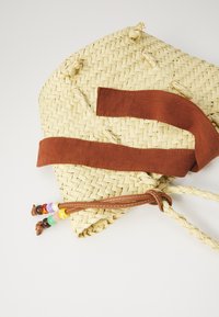 Geflochtene Strohtasche in natürlicher Farbe mit einem braunen Wildlederriemen. Verziert mit bunten Perlen an einem Lederbindeschluss.