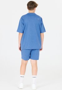 Sininen lyhythihainen t-paita ja sitä vastaavat shortsit, jotka on valmistettu pehmeästä, teksturoidusta kankaasta. Paita on väljämallinen; molemmissa vaatekappaleissa on yksinkertainen muotoilu.