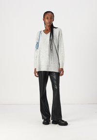 Un pull oversized gris clair avec un col en V, associé à un pantalon en simili cuir noir et des chaussures noires imposantes, accompagné d'un sac à épaule bleu.