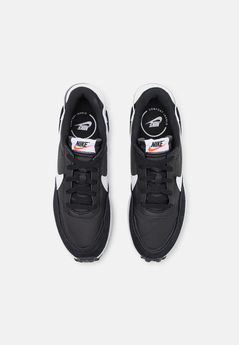 Zapatillas negras con acentos blancos, con una parte superior de tejido texturizado, diseño de cordones y una plantilla acolchada. Logo de Nike en la lengüeta.