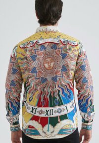 Homme aux cheveux bruns portant une chemise à manches longues colorée avec un grand visage de soleil et des chiffres romains dans le dos.