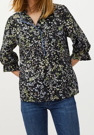 Schwarze Bluse mit floralem Muster in Grün, Blau und Weiß. Mit einer Knopfleiste und dekorativem blauen Saum am Kragen.