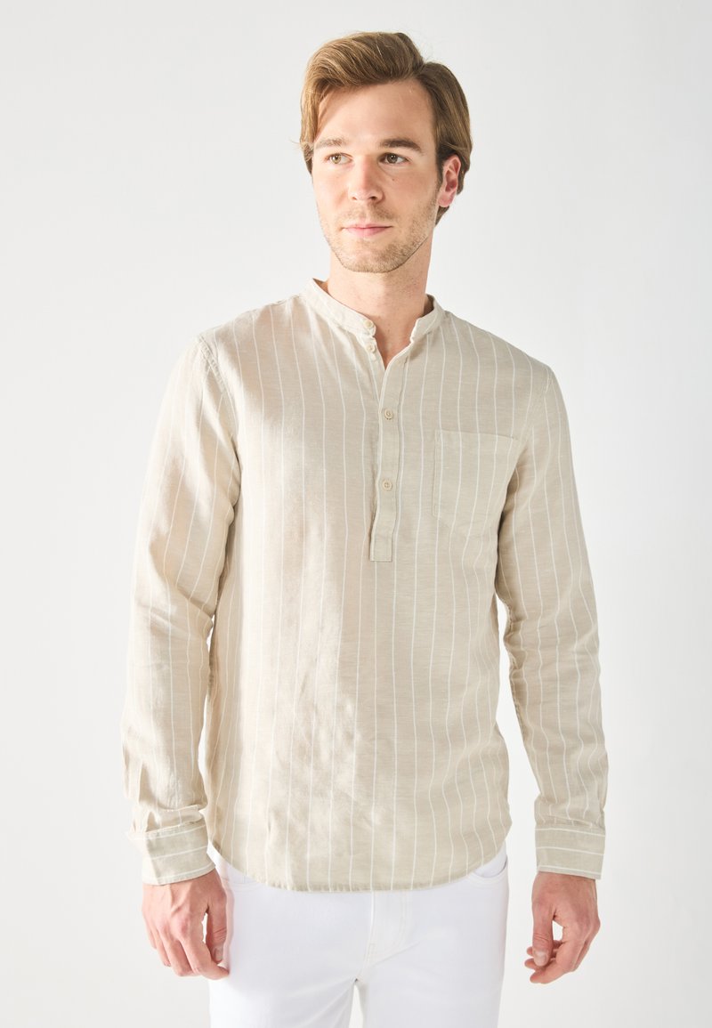 Chemise beige à manches longues avec des rayures verticales blanches, col henley boutonné et une poche sur la poitrine, fabriquée en tissu léger.